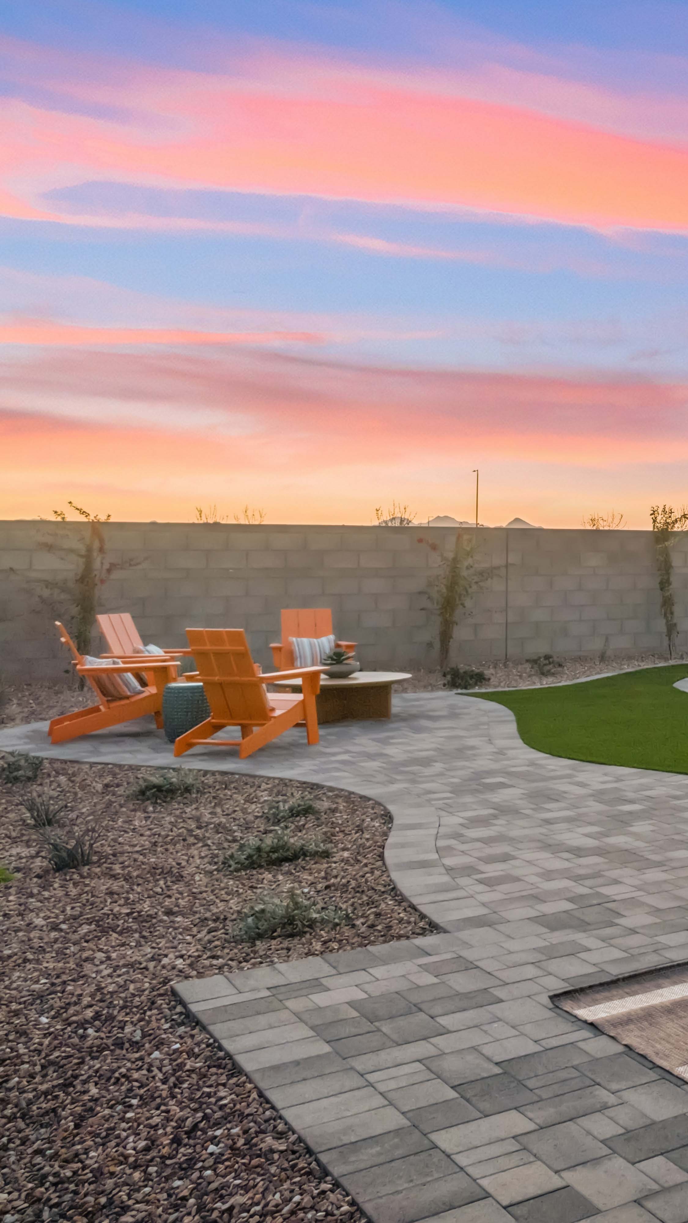 Editorial lifestyle photo detail shot backyard at sunset with airondack chairs surrounding a firepit on a paver path with turf & foliage and desert botanicals in the forground- new construction homes near Amarillo ranch palomino ranch in Maricopa AZ with USDA new construction