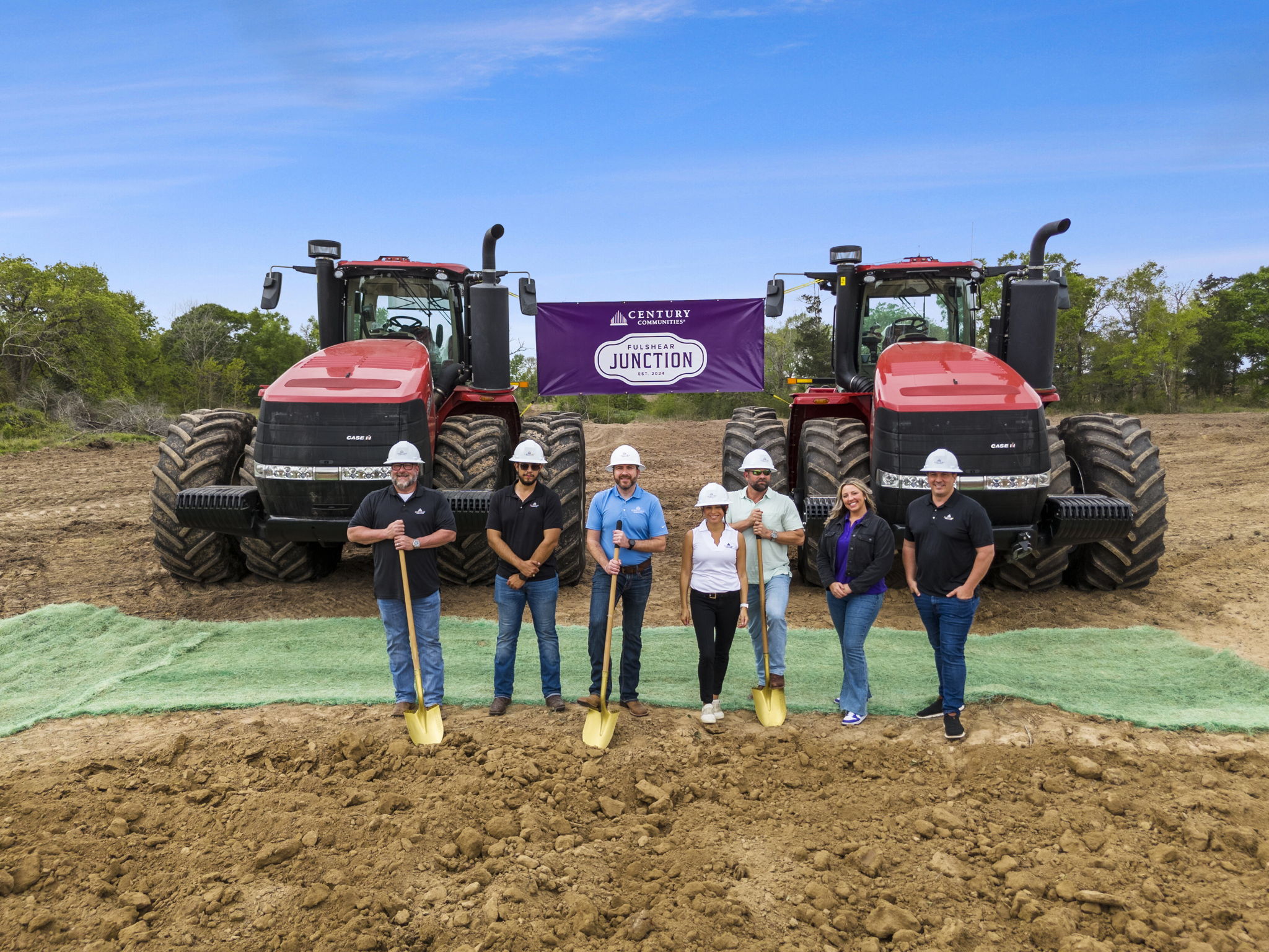 A group of people in hardhats standing in front of a tractor.