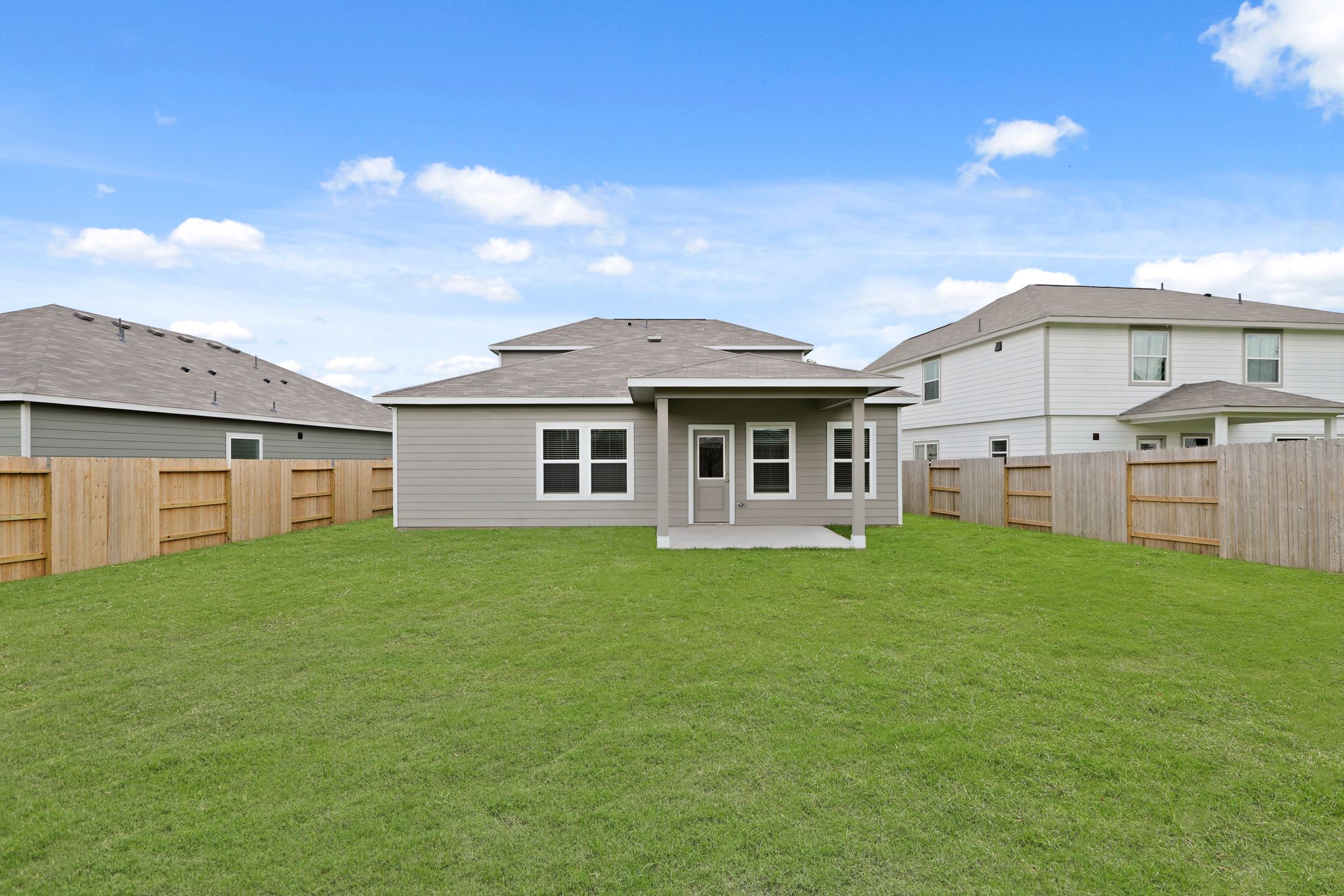 A grassy yard with a fence and houses in the background.