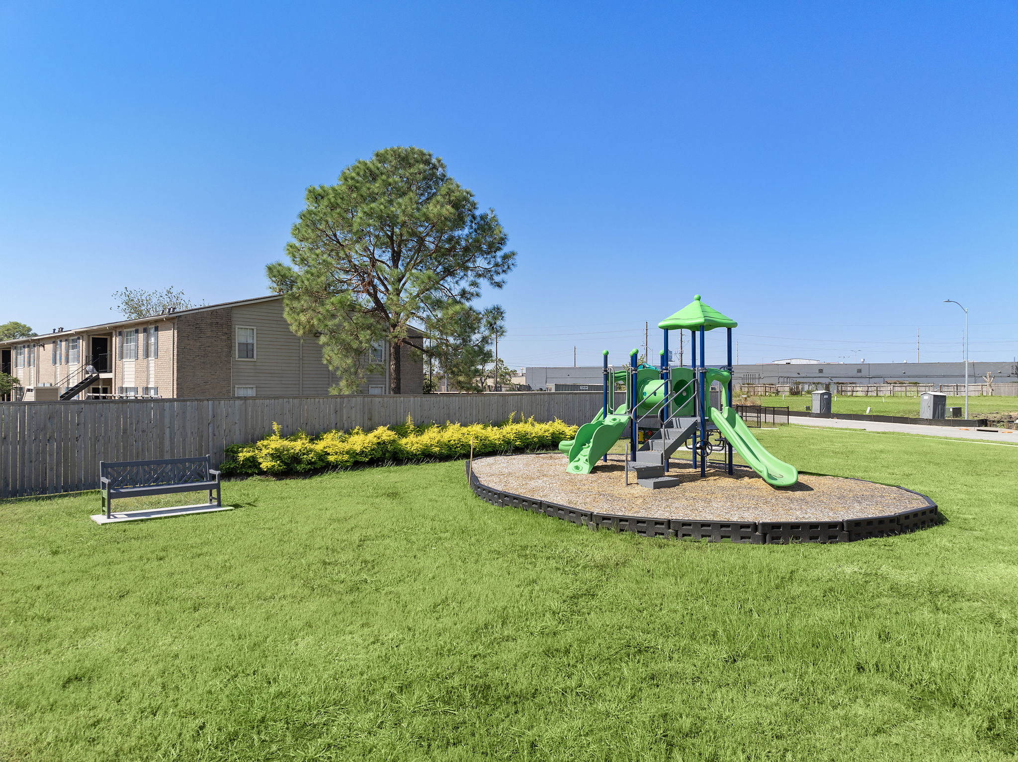 A small play structure in a grassy area with a tree and a building in the background.