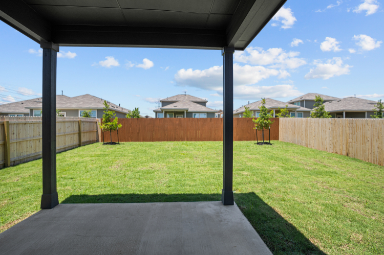 A backyard with a fence and a patio with a wood fence and trees.